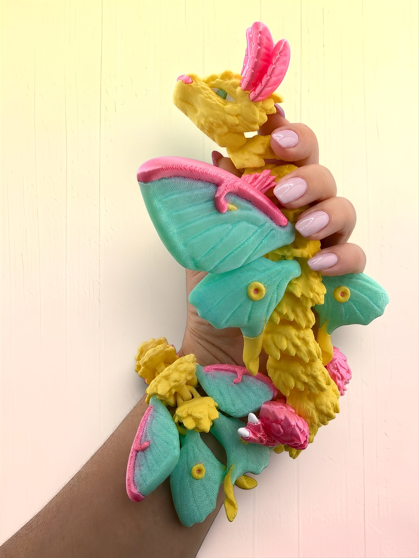 A hand holding a colorful, whimsical toy resembling a dragon or butterfly with vibrant green, pink, and yellow colors.