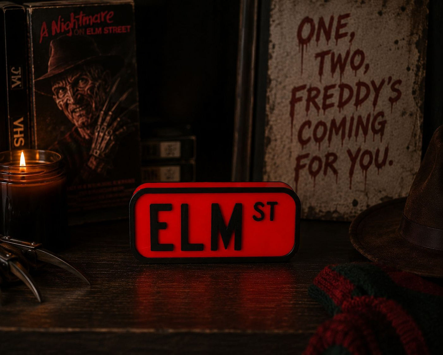 a collection of items related to the horror movie "A Nightmare on Elm Street", including a red sign with the word "ELM ST" on it, a book, a candle, and a hat.
