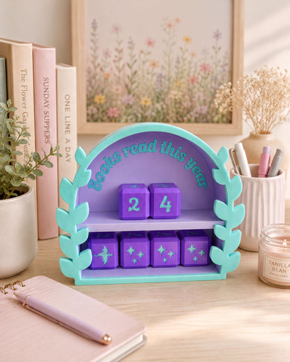 A colorful bookshelf with a purple arch and a purple book titled "Books read this year" on it, surrounded by various books, a candle, and some decorative elements.