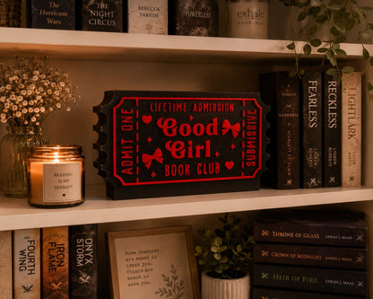 a bookshelf with various books, a candle, and a framed picture. The bookshelf has a mix of hardcover and paperback books, and there is a red ticket-shaped object on the shelf.