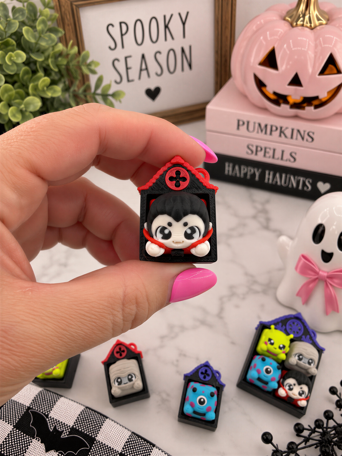 A hand holding a small black and red figurine with a face, surrounded by Halloween decorations and books.