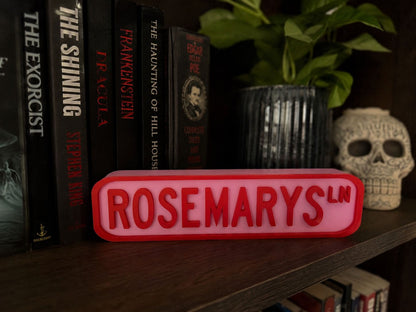 a bookshelf with several books, a skull, and a pink sign with the word "ROSEMARYS" on it.