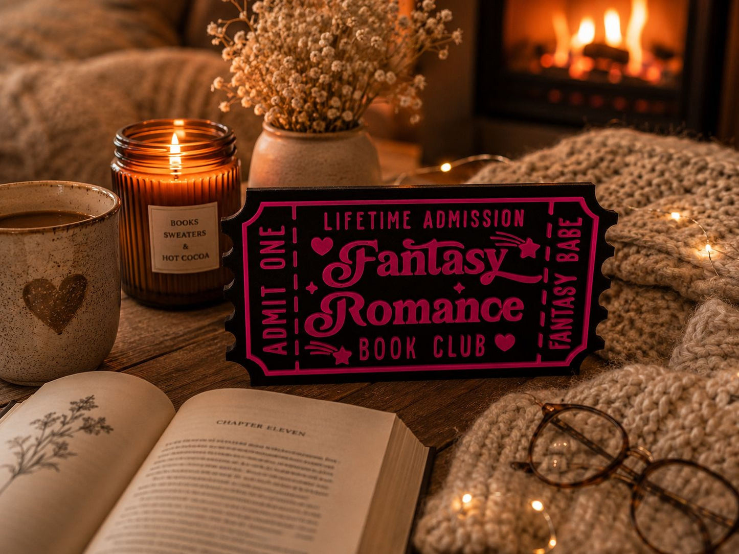a cozy scene with a fireplace, a book, a candle, and a pink sign that reads "Lifetime Admission Fantasy Romance Book Club".