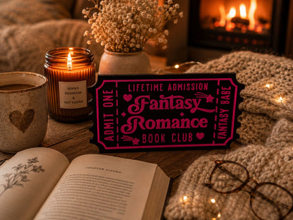 a cozy scene with a fireplace, a book, a candle, and a pink sign that reads "Lifetime Admission Fantasy Romance Book Club".