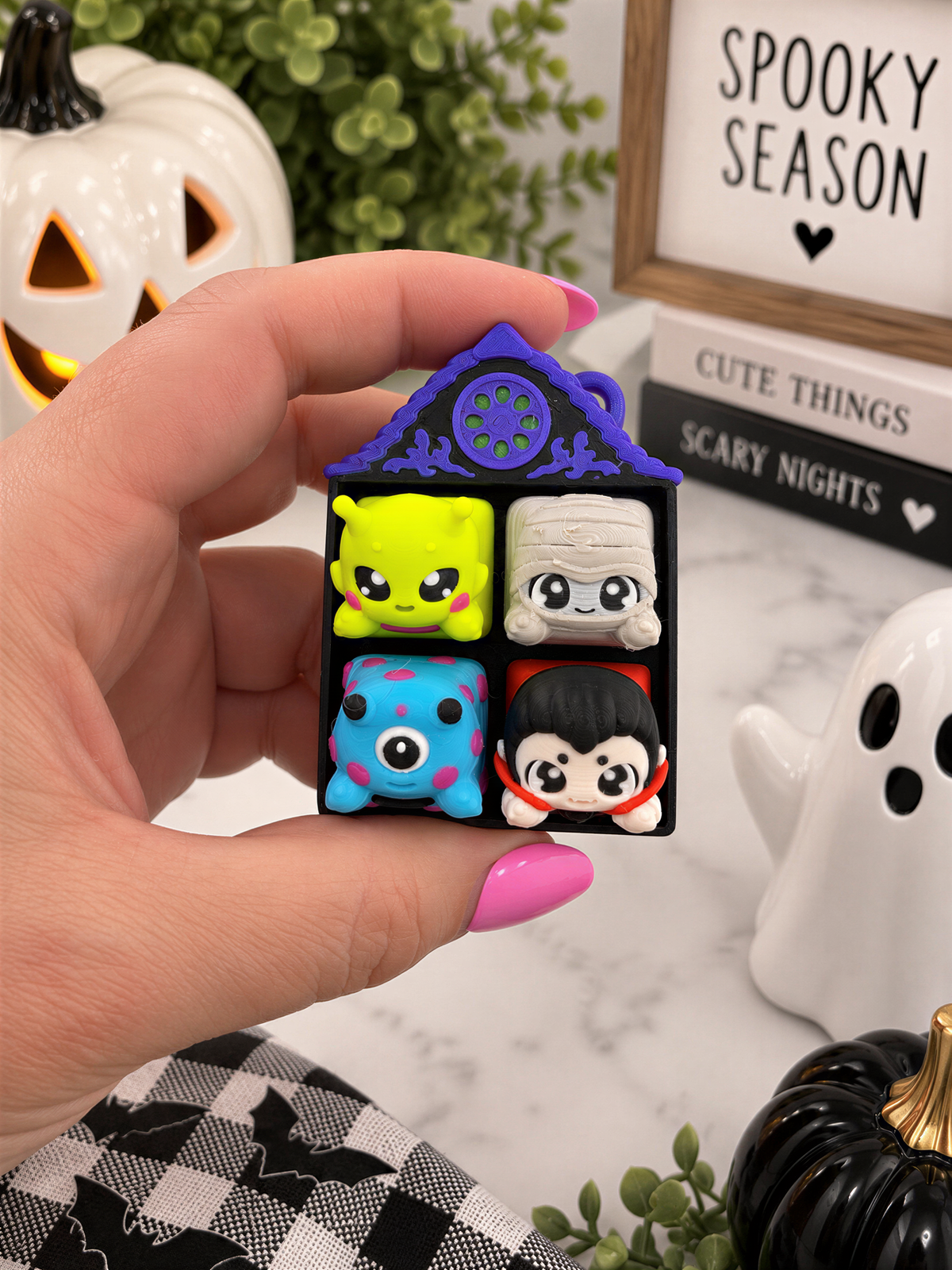 A hand holding a small toy with four different colored characters on it, surrounded by Halloween decorations and a framed sign.
