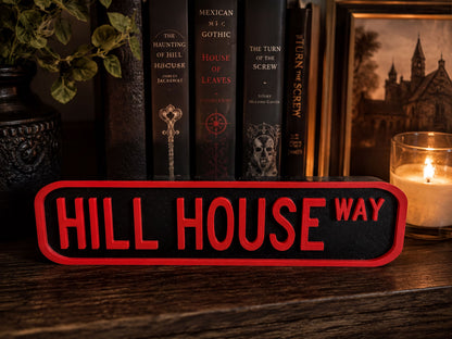 a collection of books on a shelf, with a red sign that reads "HILL HOUSE WAY" in the foreground.