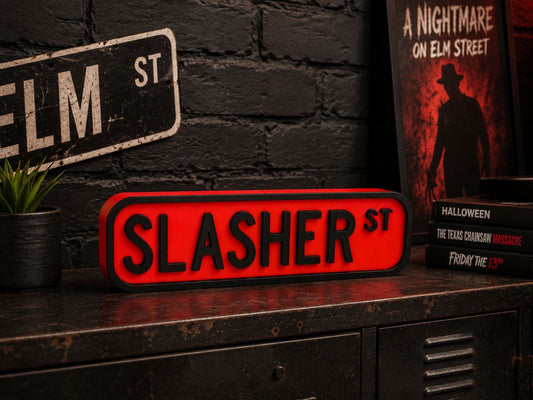 a red sign that says "SLASHER ST" on a black surface, with a book titled "A Nightmare on Elm Street" and a plant to the left.
