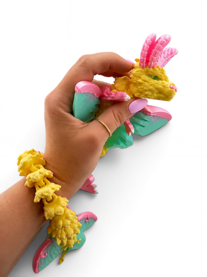 A hand is holding a colorful toy in the shape of a dragon, with a bracelet and other accessories around the toy.