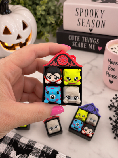 A hand holding a small toy house with various colorful characters on it, surrounded by Halloween decorations and a mug with the text "Spooky Season" on it.