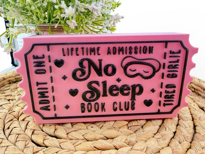 A pink ticket-shaped object with black text and graphics, placed on a woven surface.