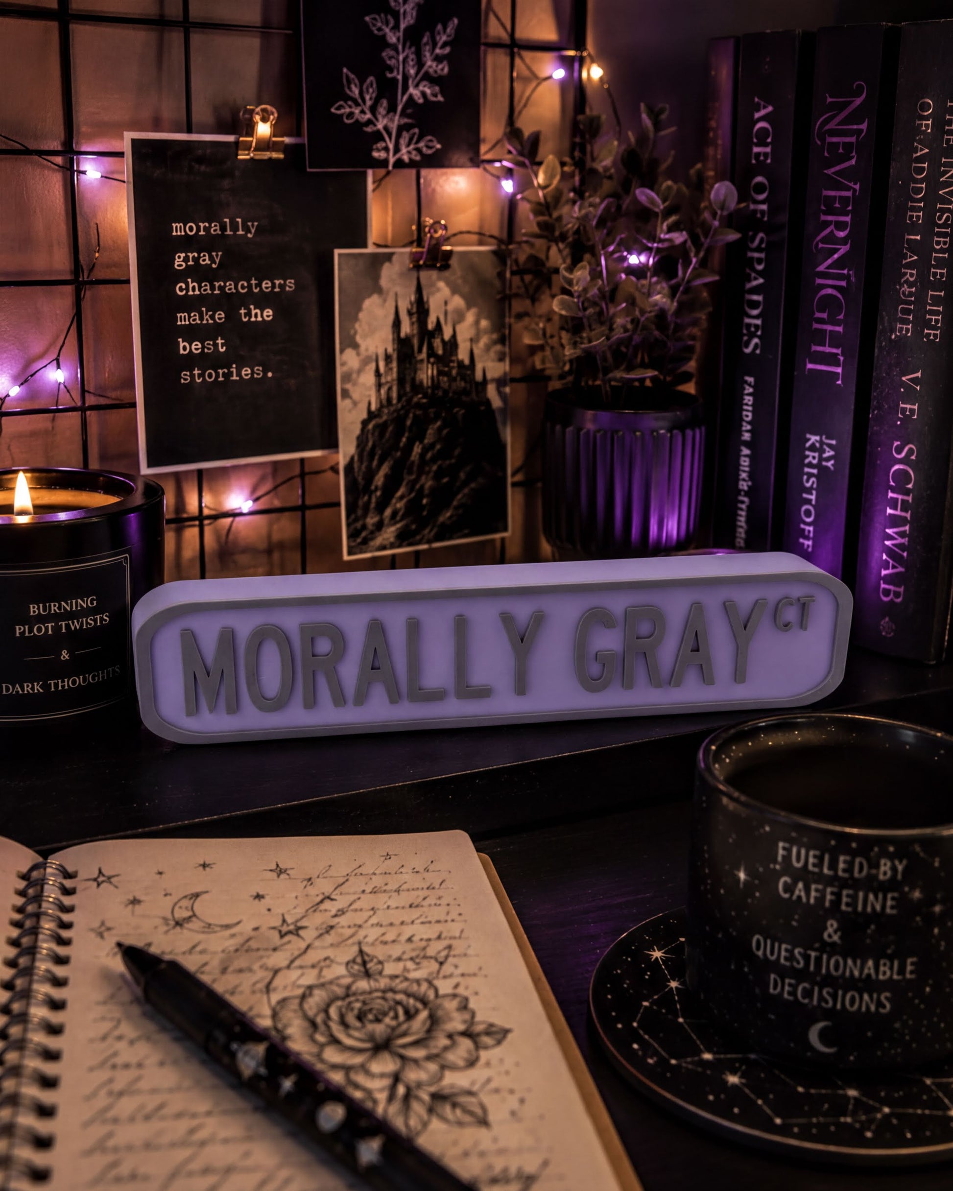 a desk with various items, including a notebook, a candle, a mug, and a sign that says "Morally Gray". There are also books and a plant on the desk.