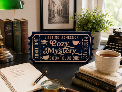 a desk with various items, including a book, a mug, a magnifying glass, and a ticket-shaped sign that reads "Cozy Mystery Book Club".