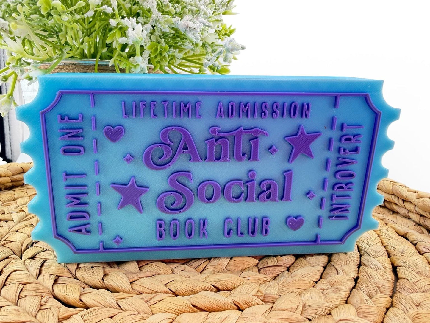 A blue ticket-shaped object with purple text, sitting on a woven mat.