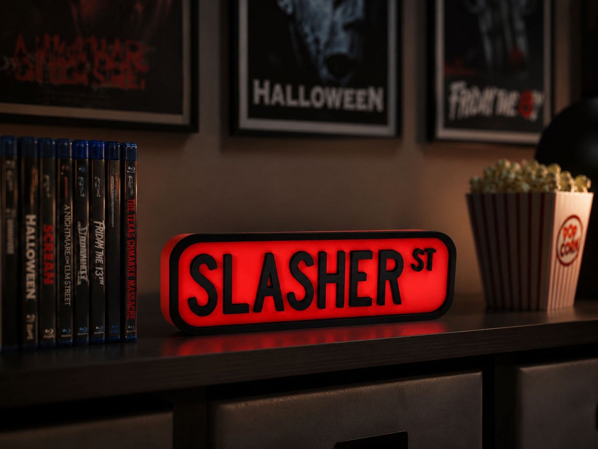 a shelf with a collection of horror movie DVDs, a red sign that says "SLASHER ST", and a popcorn bucket.
