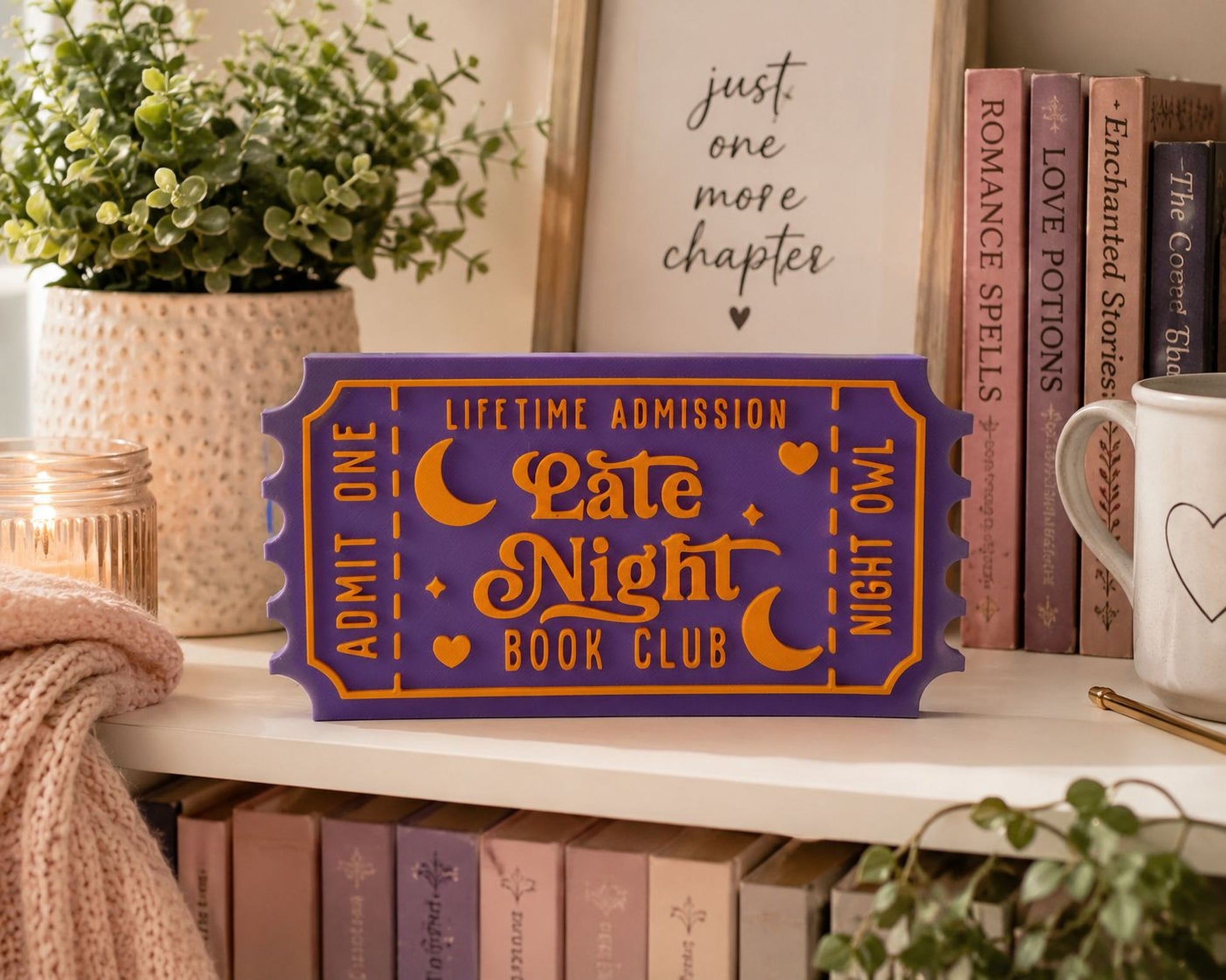 a purple ticket-shaped sign with orange and white text, placed on a shelf among books and a plant.