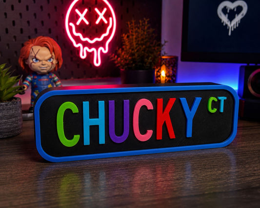 A colorful sign with the word "CHUCKY" in large letters, surrounded by various objects such as a doll, a neon sign, and a plant.