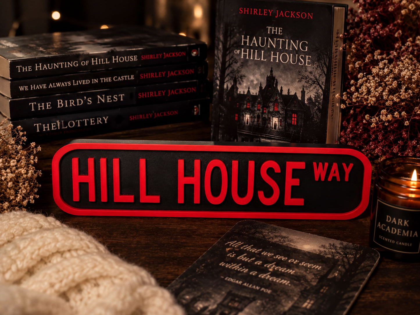 a collection of books and a sign that reads "HILL HOUSE WAY", along with a candle and some decorative elements.