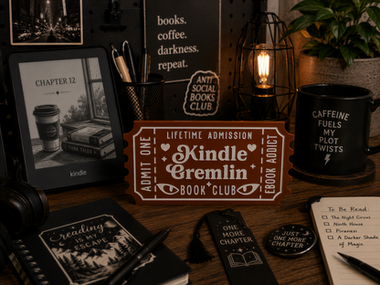 a desk with various items, including a Kindle e-reader, a mug, a notebook, a pen, and a plant. The desk also has a sign that says "Lifetime Admission Kindle Cremlin Book Club".