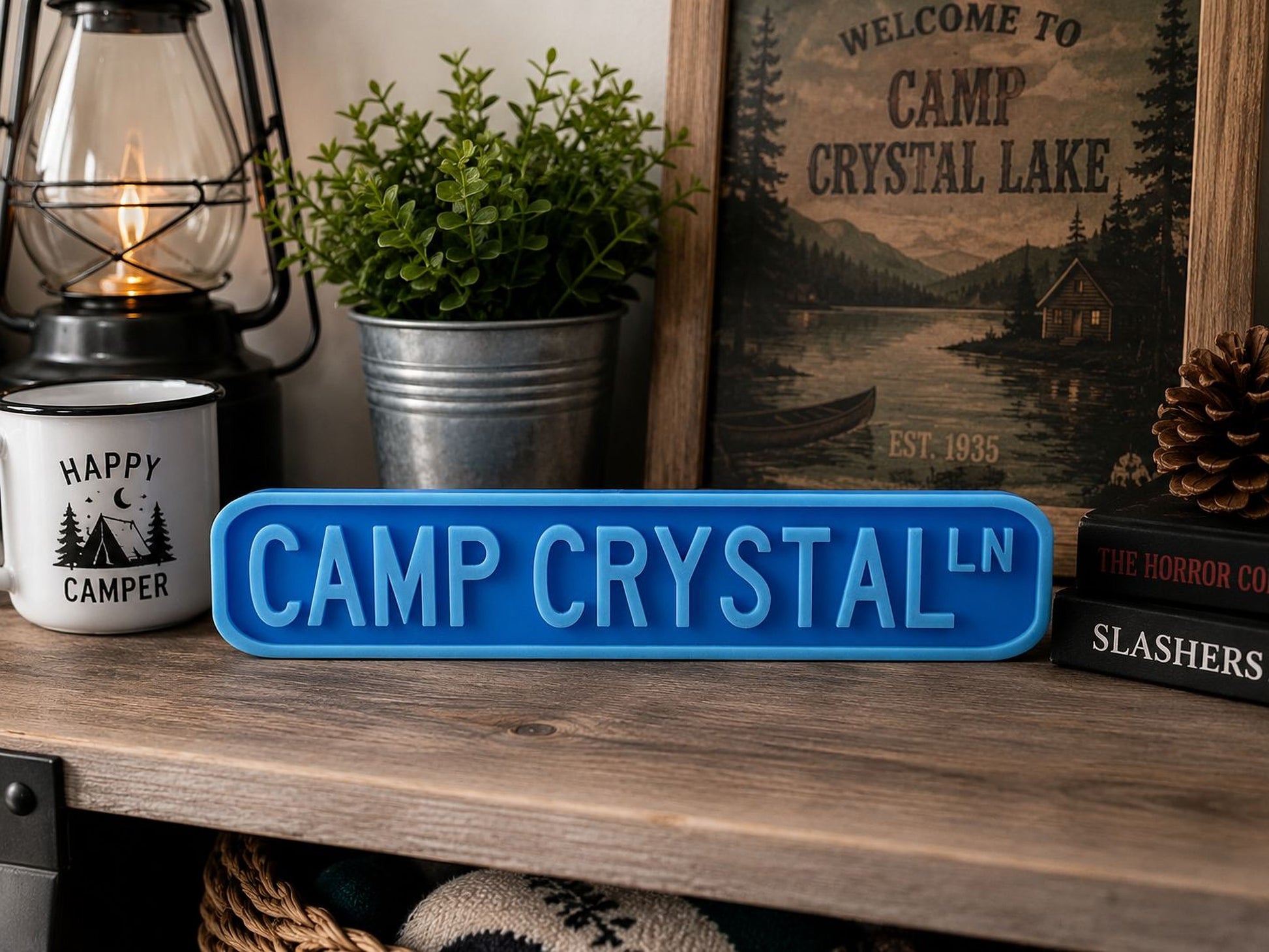 a wooden shelf with various items, including a blue sign that says "CAMP CRYSTAL", a lantern, a potted plant, and a framed picture of a cabin.