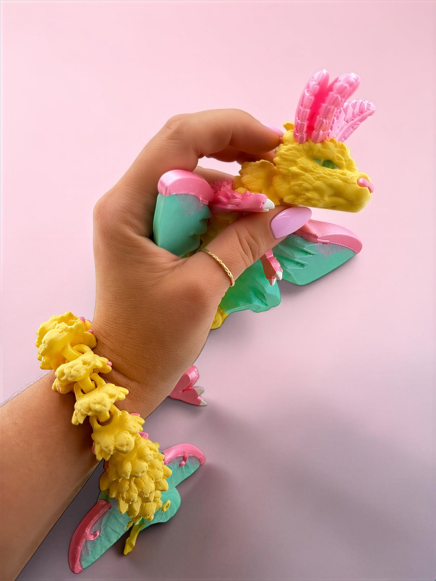 A hand is holding a colorful toy in a pink and green color scheme, with the toy's head and body visible.
