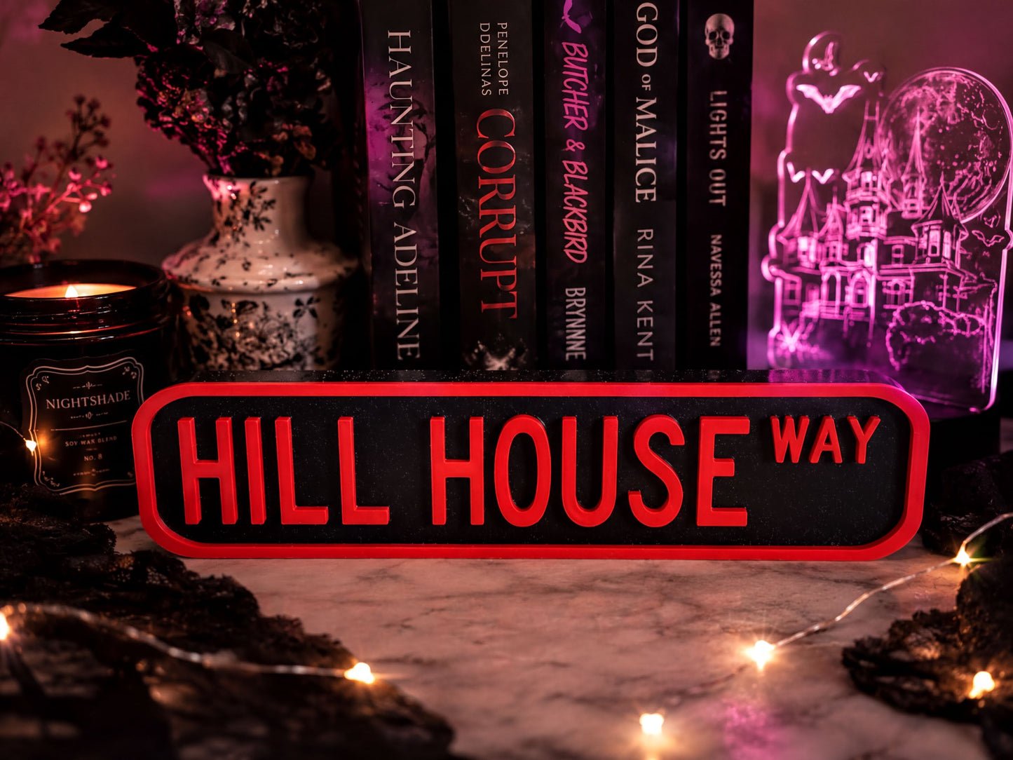 a collection of books, a candle, and a sign that reads "Hill House Way" in a dark and moody setting.