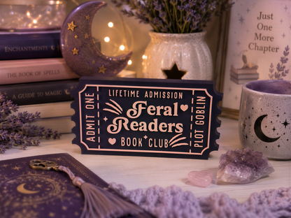 a book club ticket, a mug with a crescent moon design, and various books and decorative items arranged on a table.