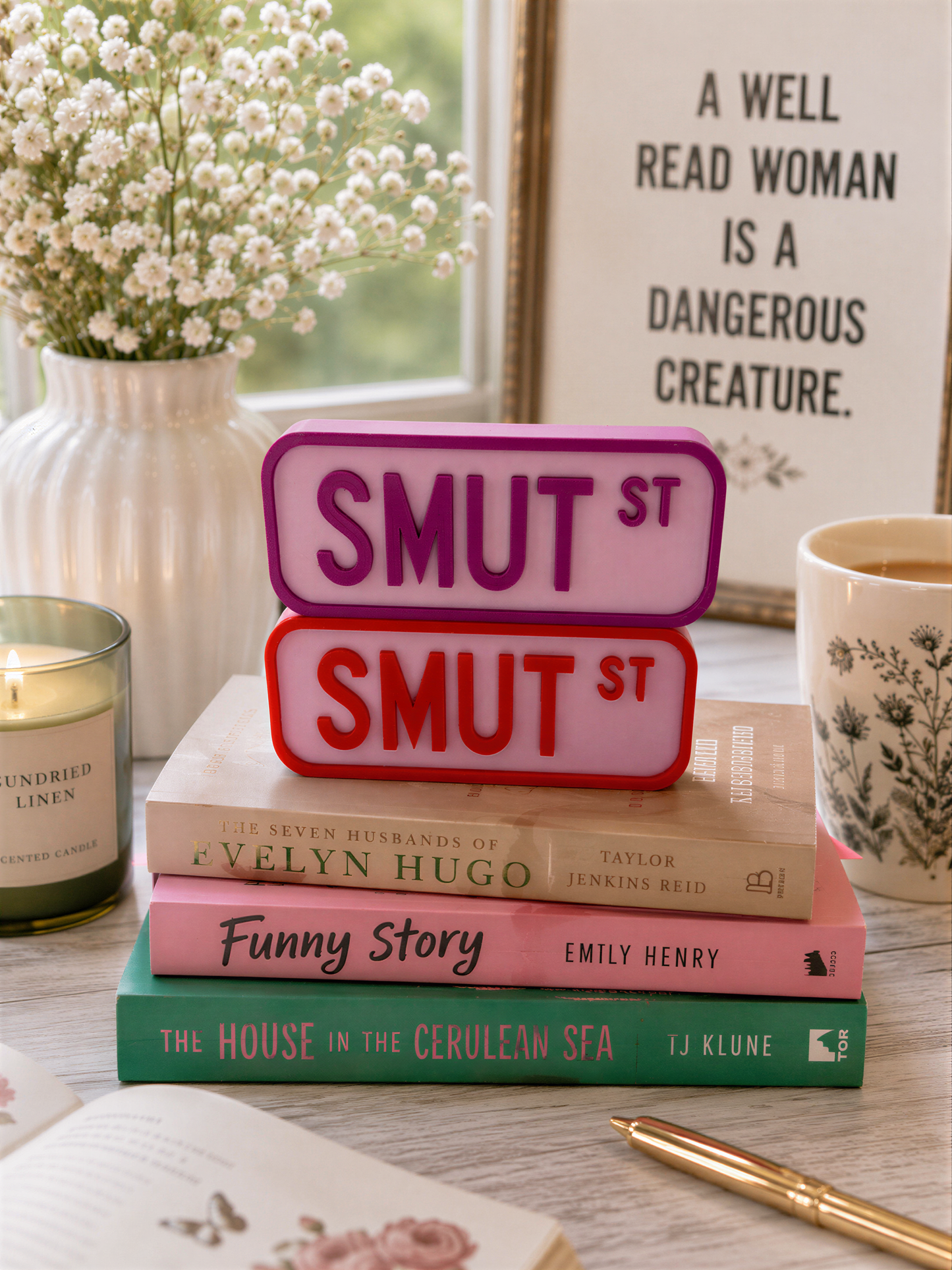 a stack of books, a vase with flowers, a candle, and a framed quote on a table.