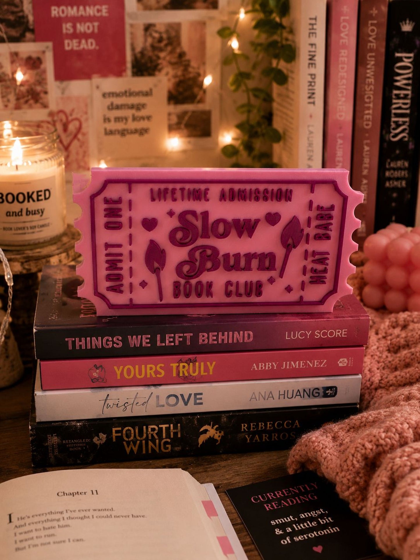 a stack of books, a pink ticket-shaped object, and some candles on a table.