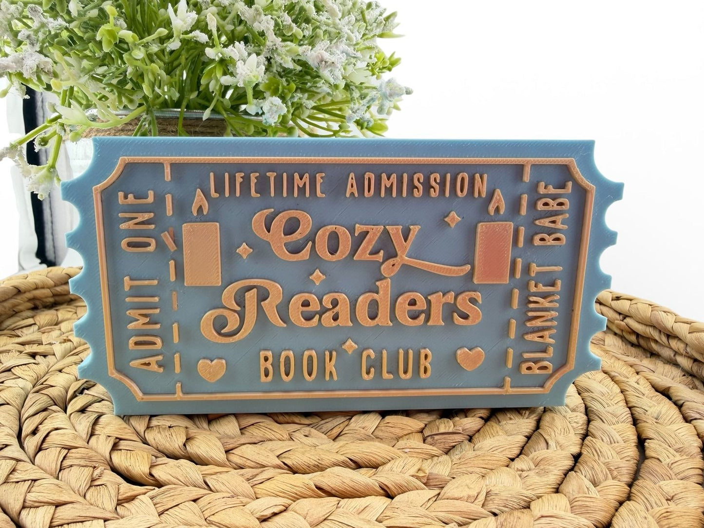 A blue and orange ticket-shaped sign for a "Cozy Readers Book Club" with the text "Lifetime Admission" and "Book Club" printed on it.