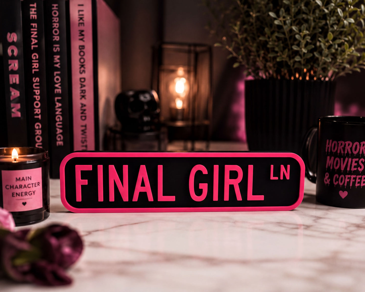 a pink sign that says "FINAL GIRL LN" in bold letters, surrounded by various objects such as a candle, a mug, and a potted plant.