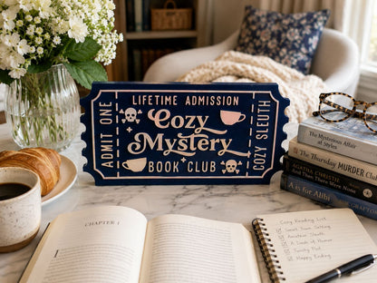 a cozy reading setup with a book club sign, a notebook, a pen, a cup of coffee, and a stack of books on a table.