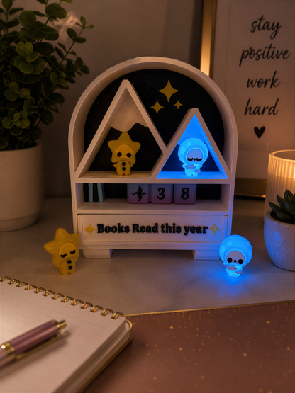 A white and black desk lamp with a blue light, featuring a small figurine and a clock, sits on a desk next to a notebook and a pen.