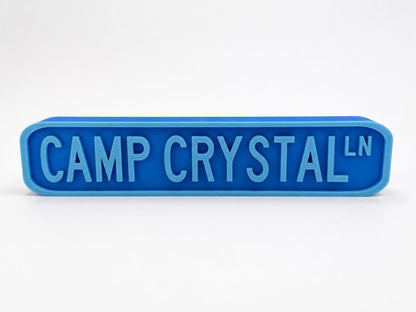 A blue rectangular sign with the text "CAMP CRYSTAL" in large letters.