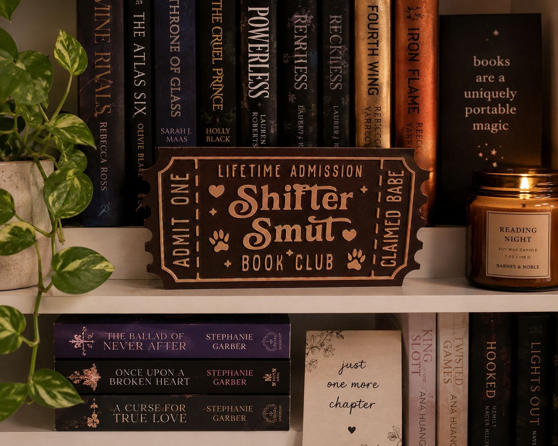 a bookshelf filled with various books, a candle, and a sign that reads "Shifter Smut Book Club".