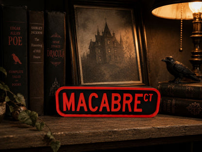 a bookshelf with several books, a framed picture of a castle, a black bird figurine, and a red sign with the word "MACABRE" on it.