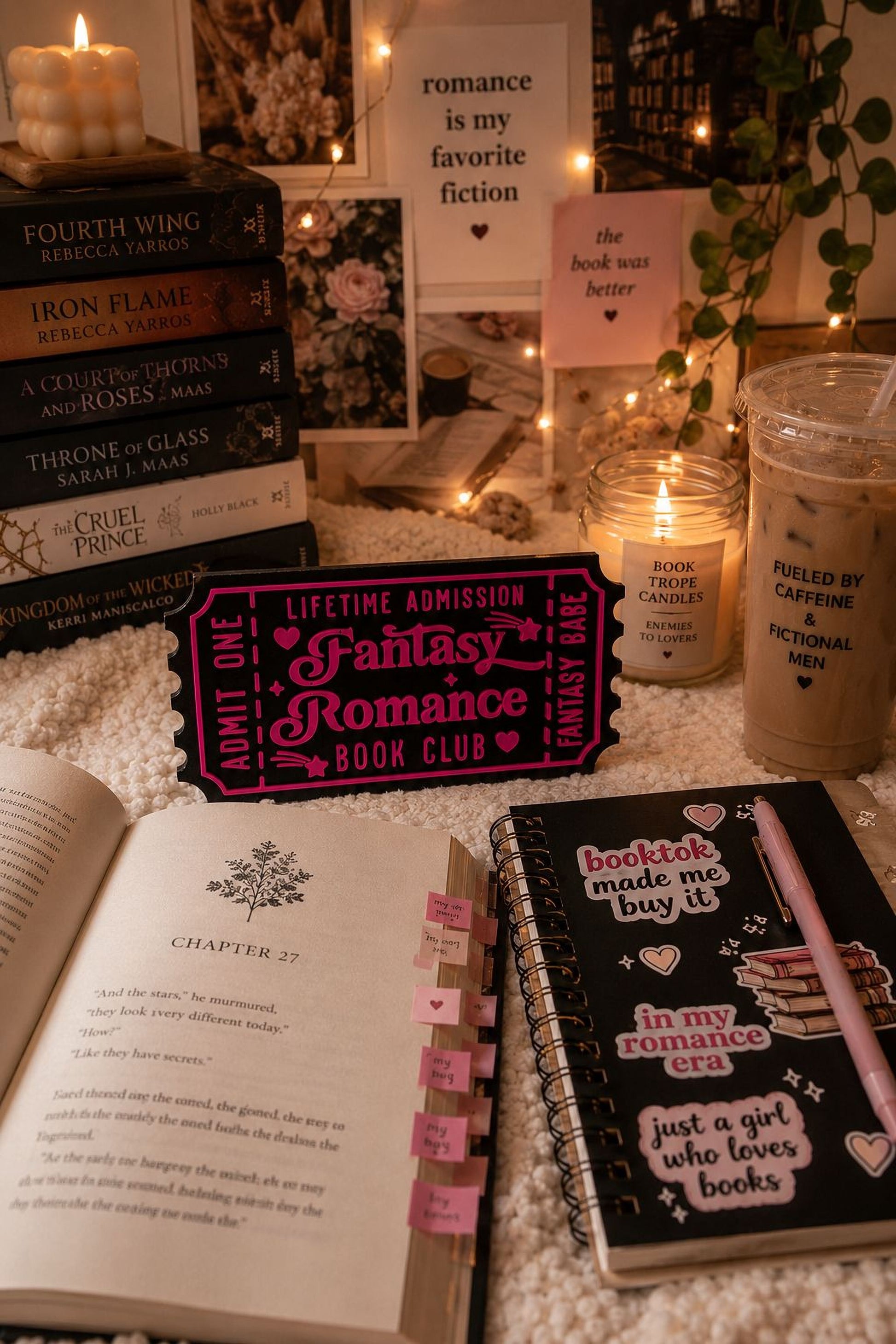a cozy scene with a stack of romance novels, a pink ticket-shaped bookmark, a notebook, and a candle, all arranged on a bed with a white blanket.