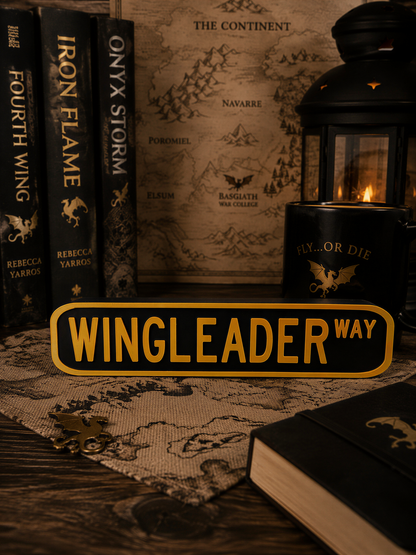 a collection of books, a map, a lantern, and a sign that reads "WINGLEADER WAY", all arranged on a wooden surface.