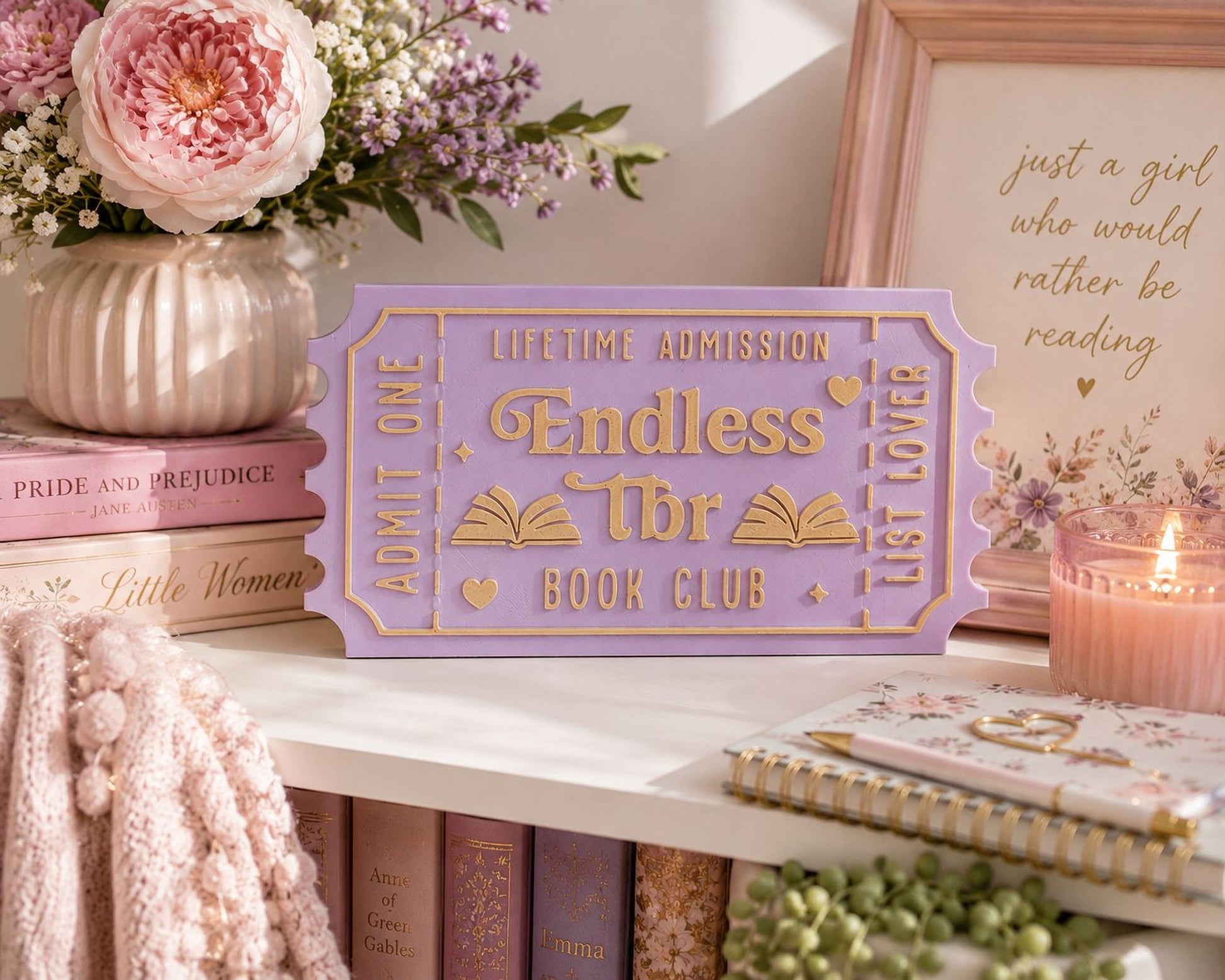a purple book club sign with gold lettering, surrounded by various books, a vase of flowers, and a candle on a shelf.
