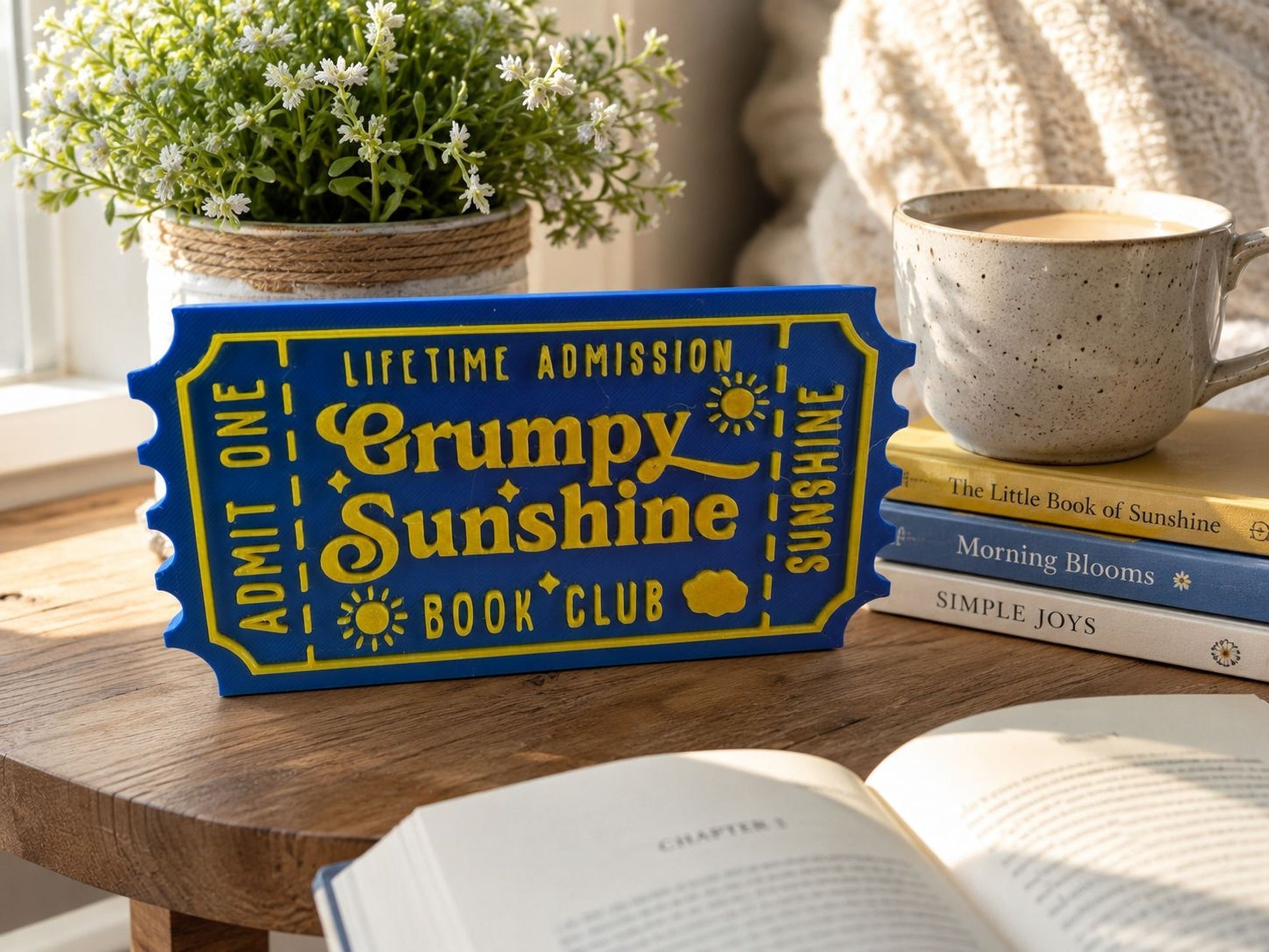 a blue ticket-shaped sign with yellow text, placed on a wooden table next to a stack of books and a mug.