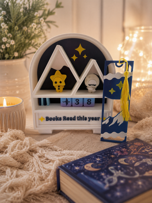 a bookshelf with a book titled "Books Read this year", a small figurine of a star, and a decorative bookmark. The bookshelf is placed on a table with a candle and a vase of flowers.