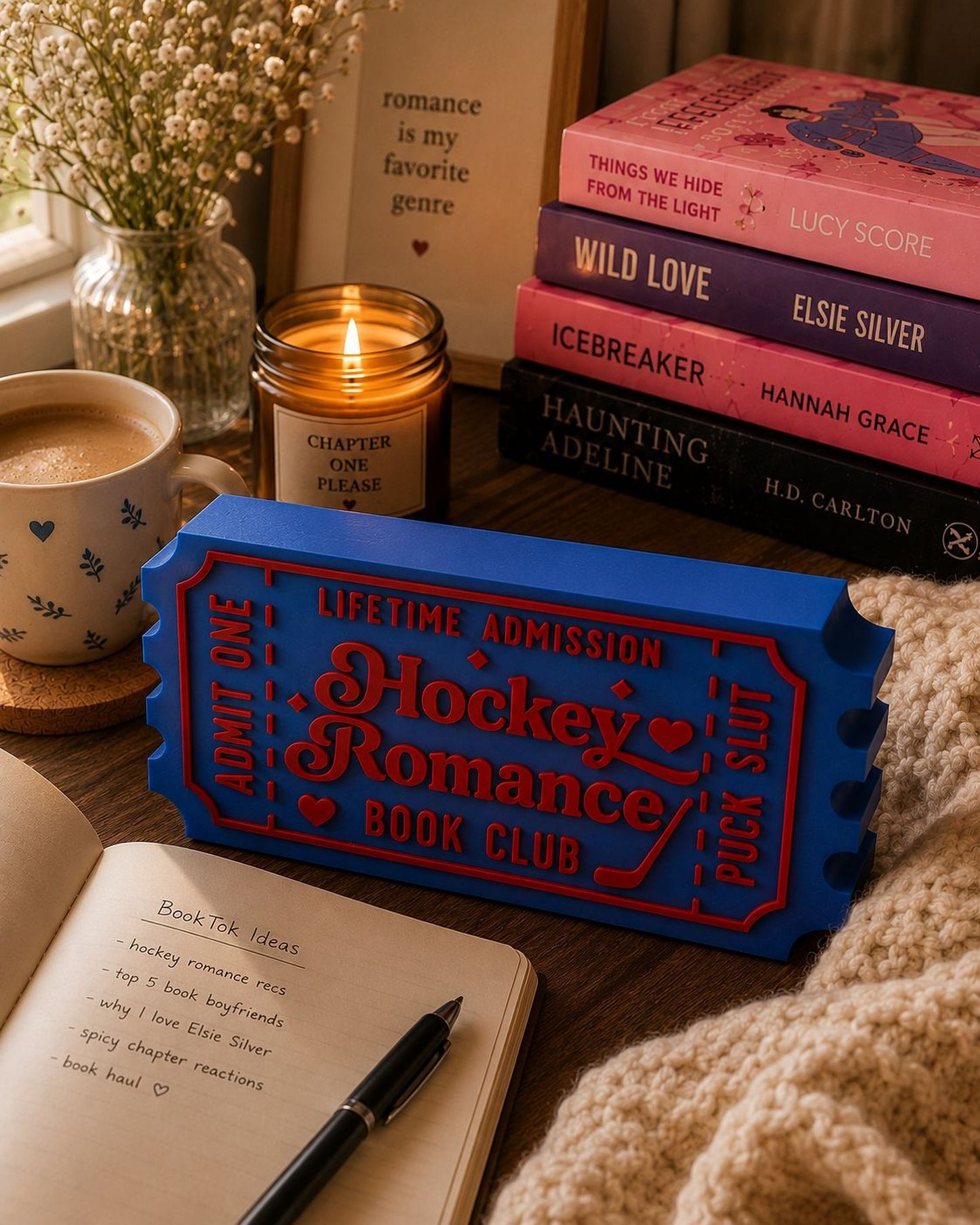 a cozy scene with a candle, a mug, a notebook, and a stack of books on a table.
