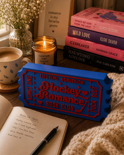 a cozy scene with a candle, a mug, a notebook, and a stack of books on a table.