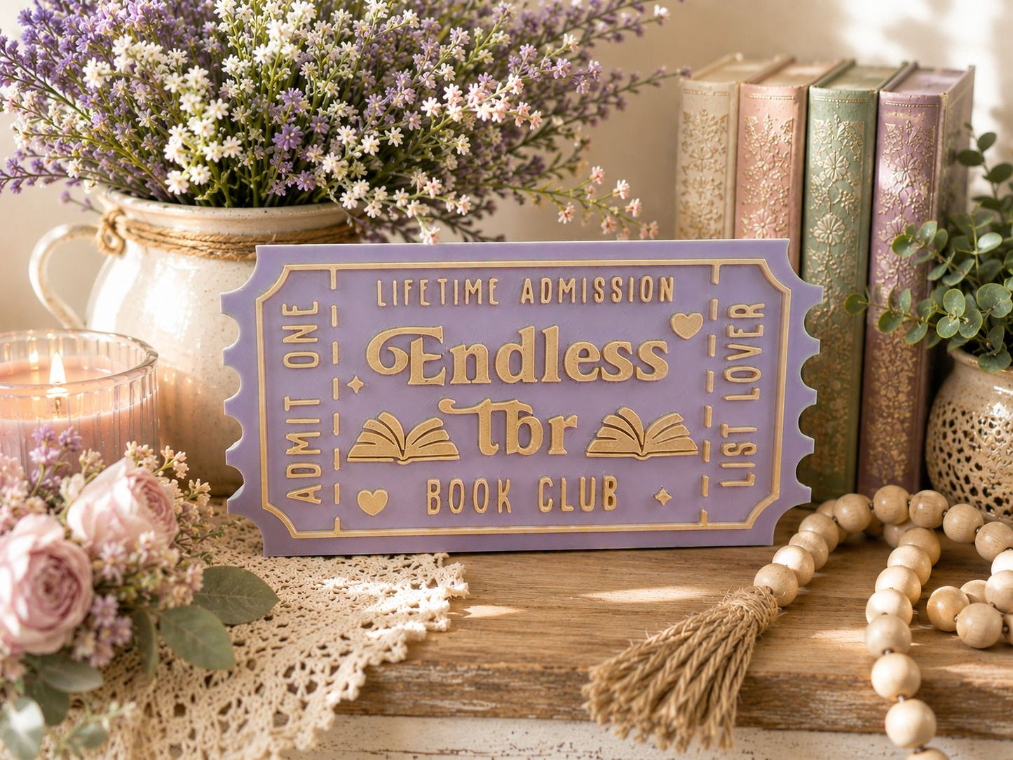 a purple ticket-shaped sign with gold lettering, surrounded by various decorative items such as books, flowers, and a beaded string.