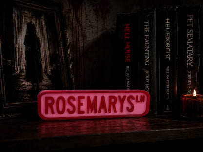 a dark, spooky scene with a red sign that reads "ROSEMARYS.LN" in the foreground, surrounded by a collection of horror books and a lit candle.