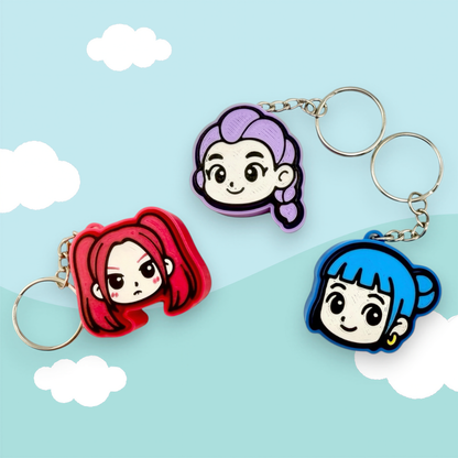 three keychains with cartoon-style female characters on them, set against a light blue sky with clouds.