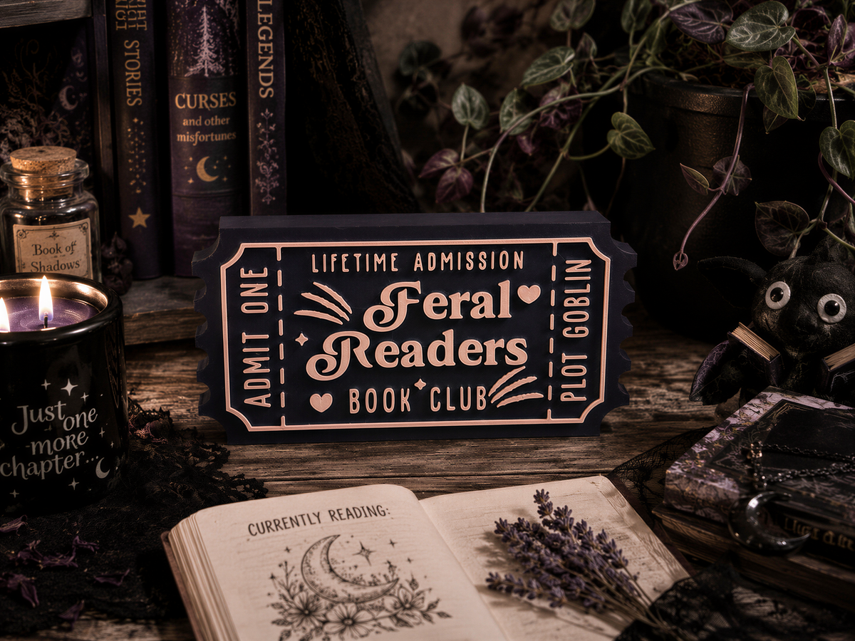 a book club sign for "Feral Readers" with a candle, a stuffed animal, and various books and items surrounding it.