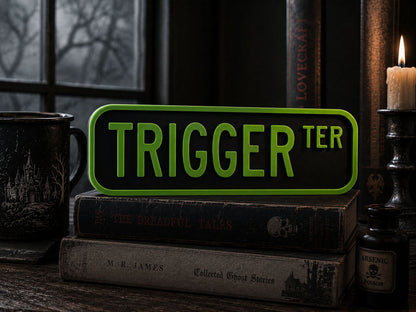 a stack of books, a mug, and a candle, with a green sign that says "TRIGGER TER" in the foreground.