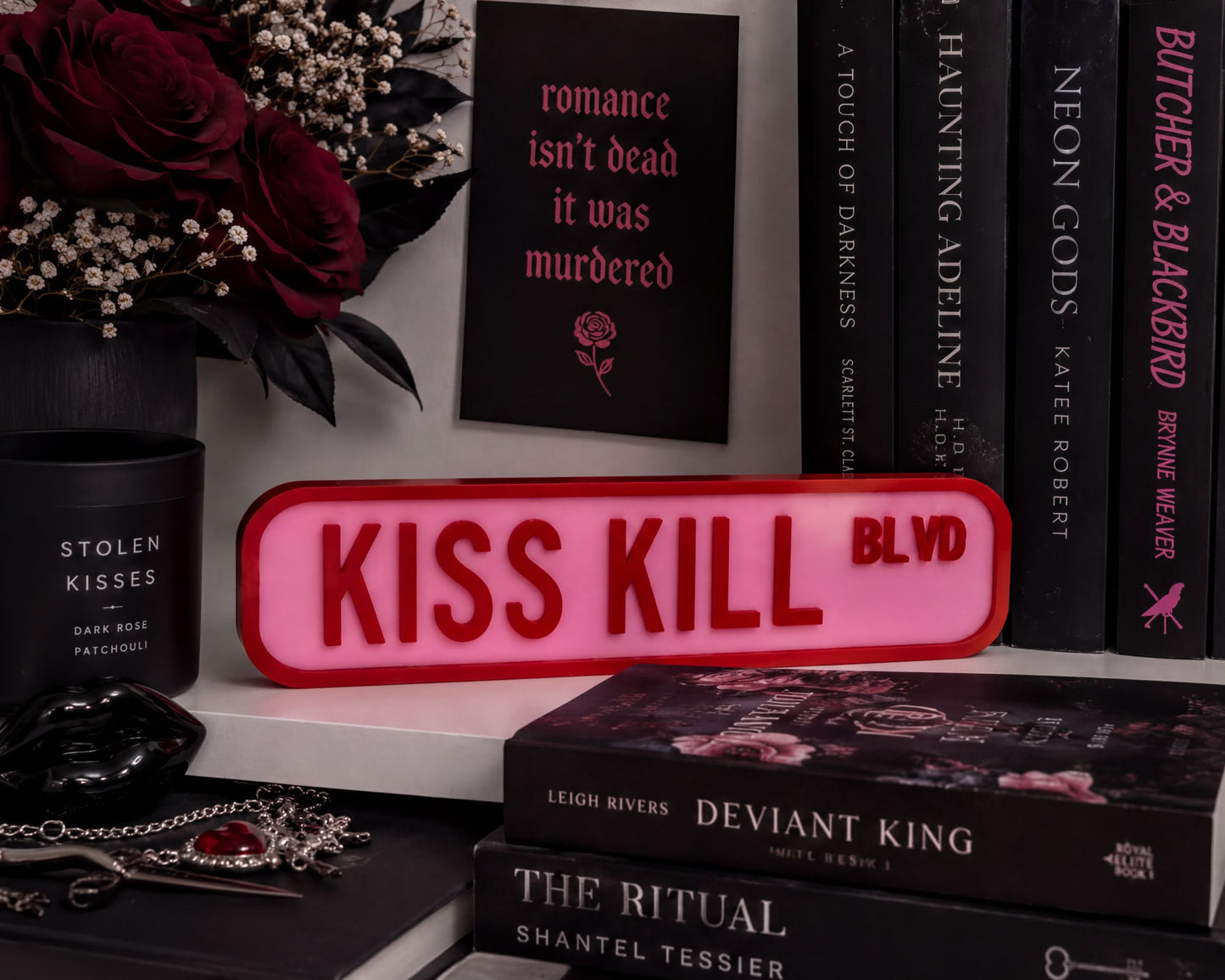 a collection of books, a pink sign, and some flowers arranged on a shelf.
