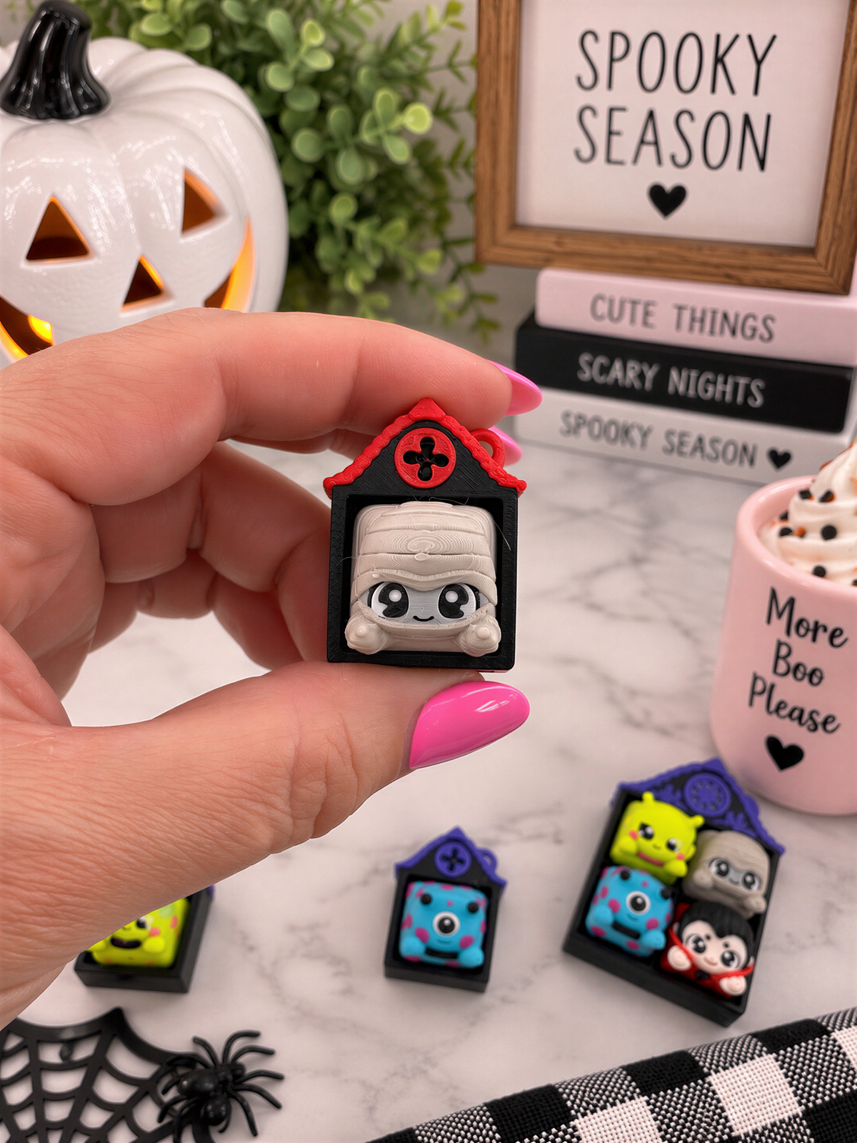 A hand holding a small toy resembling a house with a face, surrounded by Halloween decorations and books.