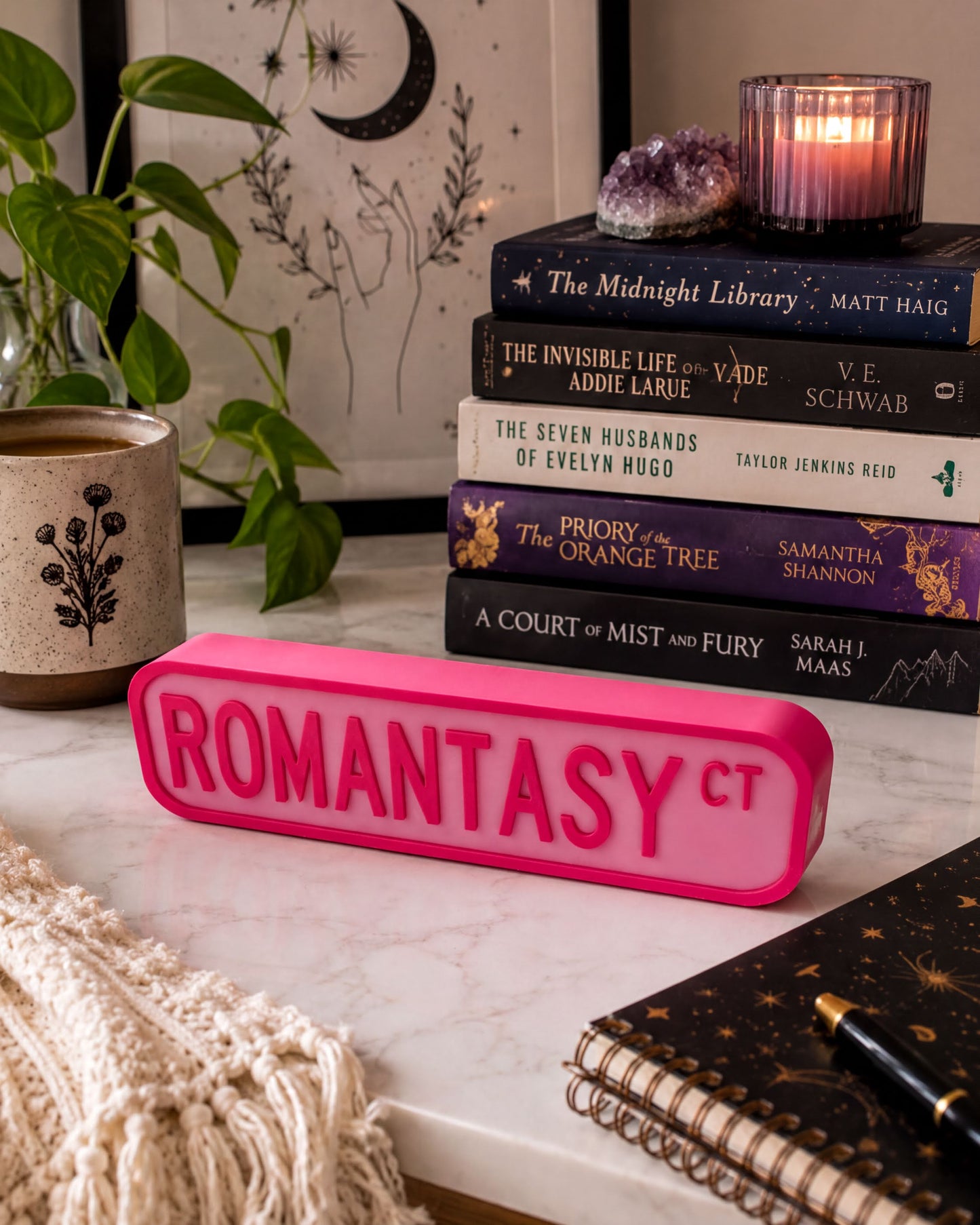 a collection of books, a pink object, and some decorative elements arranged on a white marble surface.